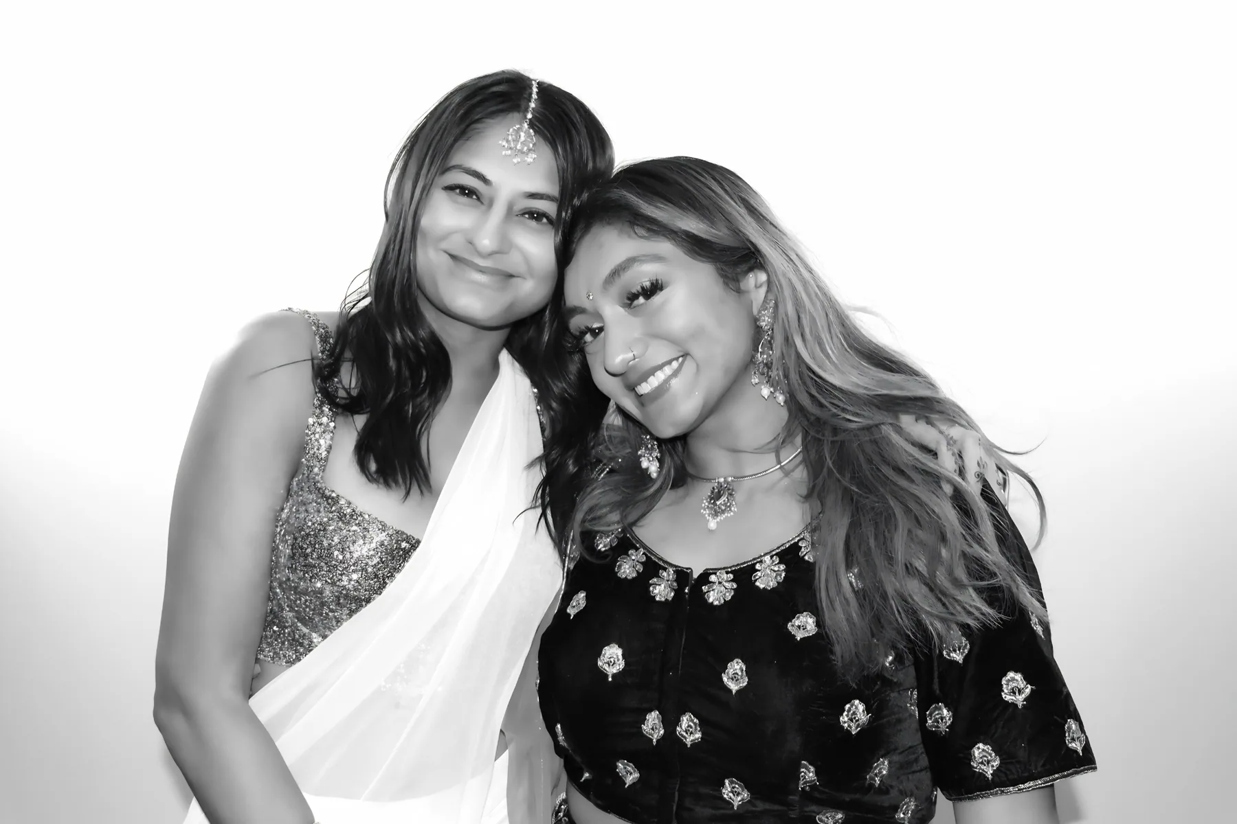 Two women in traditional attire smiling in a black and white Glam Booth photo
