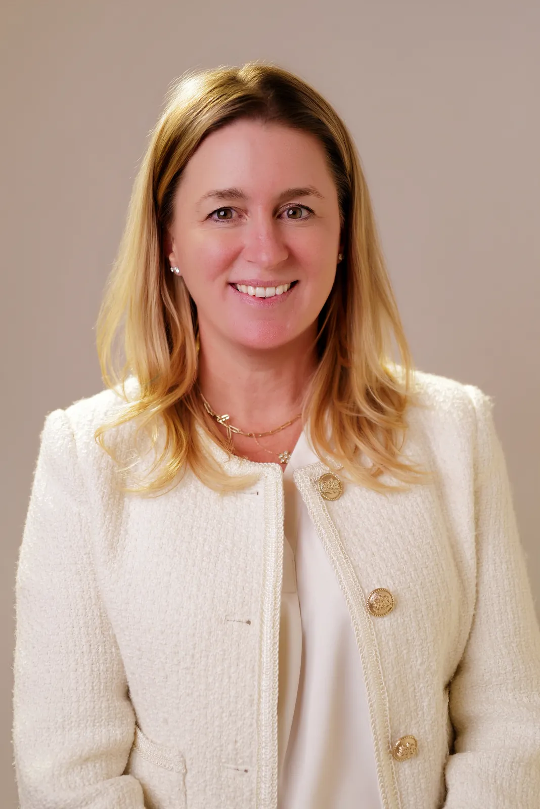 Studio headshot of a smiling blonde woman in a cream tweed jacket